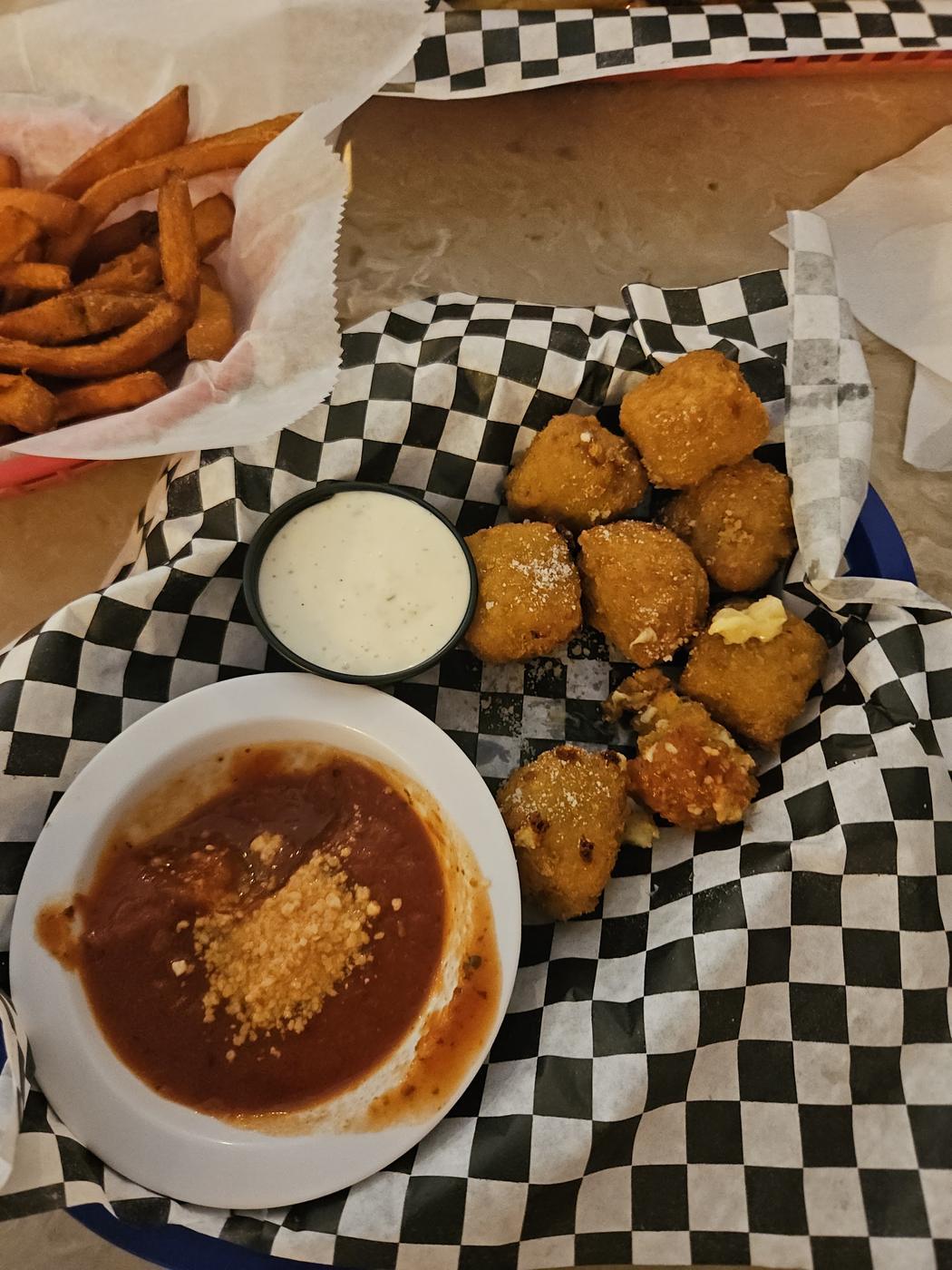 A basket of breaded fried bites with marinara and ranch, and a basket of sweet potato fries